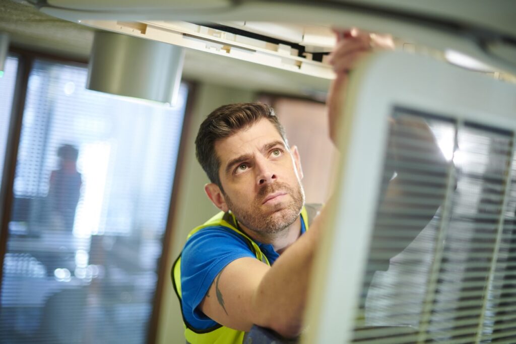 24/7 Emergency Heating Repair for Urgent Situations 10 A man in a safety vest repairs an air conditioner on a building rooftop.